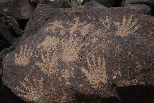 Image of human hand petroglyphs carved on dark volcanic rock at Petroglyph National Monument, New Mexico.